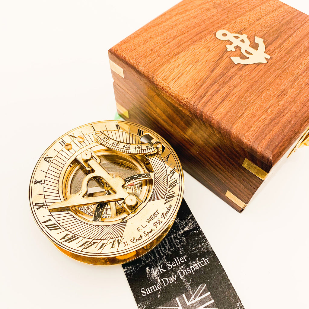 May include: A brass sundial with Roman numeral markings and a compass rose. The sundial is in a wooden box with a brass anchor on the lid. The box is closed.
