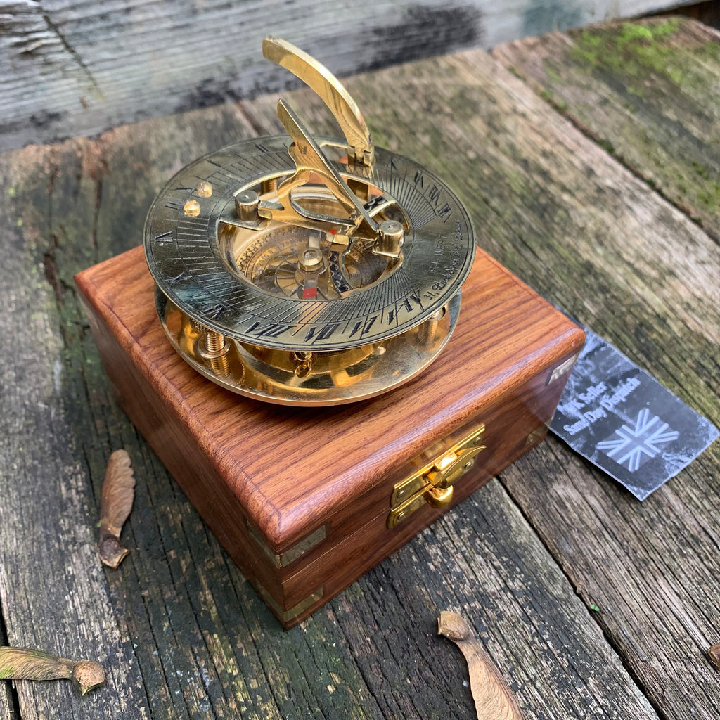 Puede incluir: Un reloj de sol de latón con brújula, colocado sobre una caja de madera. El reloj de sol tiene números romanos y un gnomon con bisagras. La caja es de madera oscura con herrajes de latón. Una etiqueta con el texto "UK Seller Same Day Dispatch" es visible.