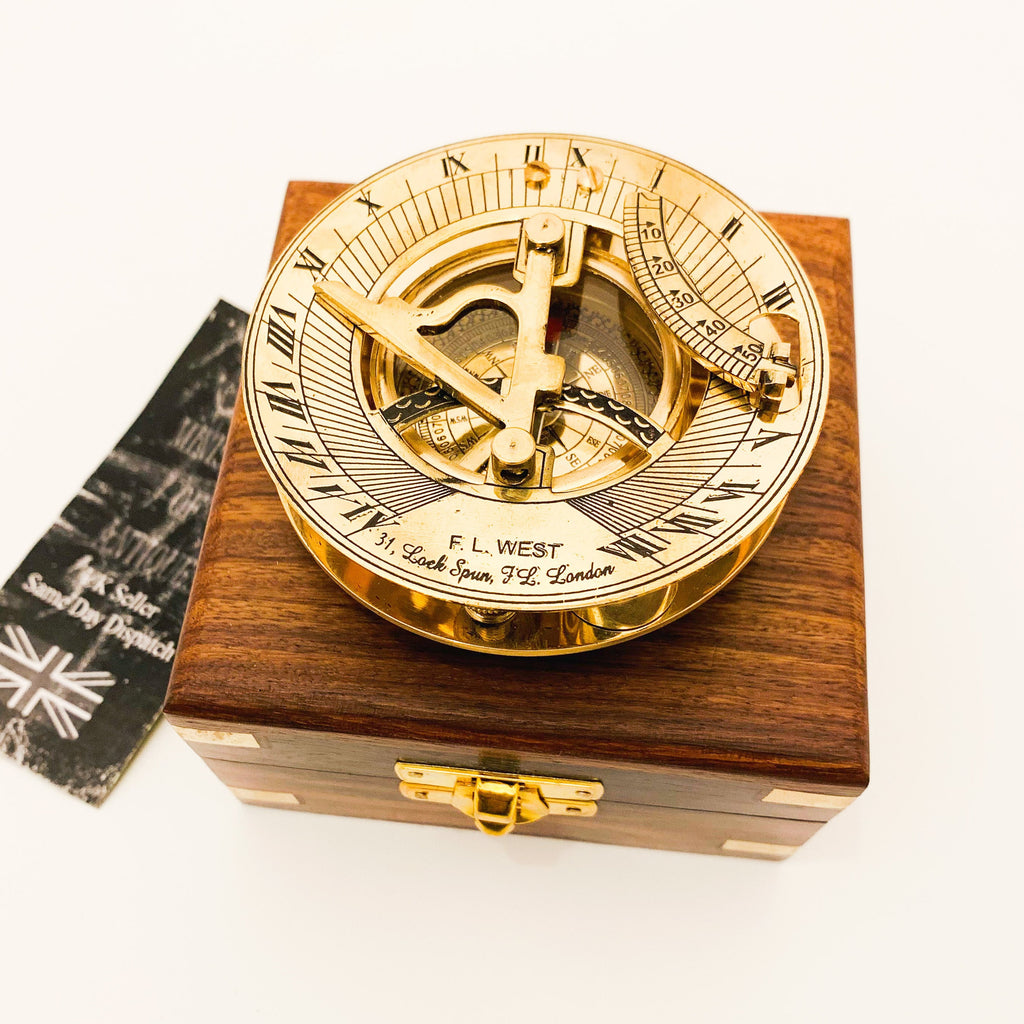 May include: A brass sundial compass in a wooden box. The compass has a gold finish and is engraved with the words "F.L. WEST 31, Lock Spun, FL. London".