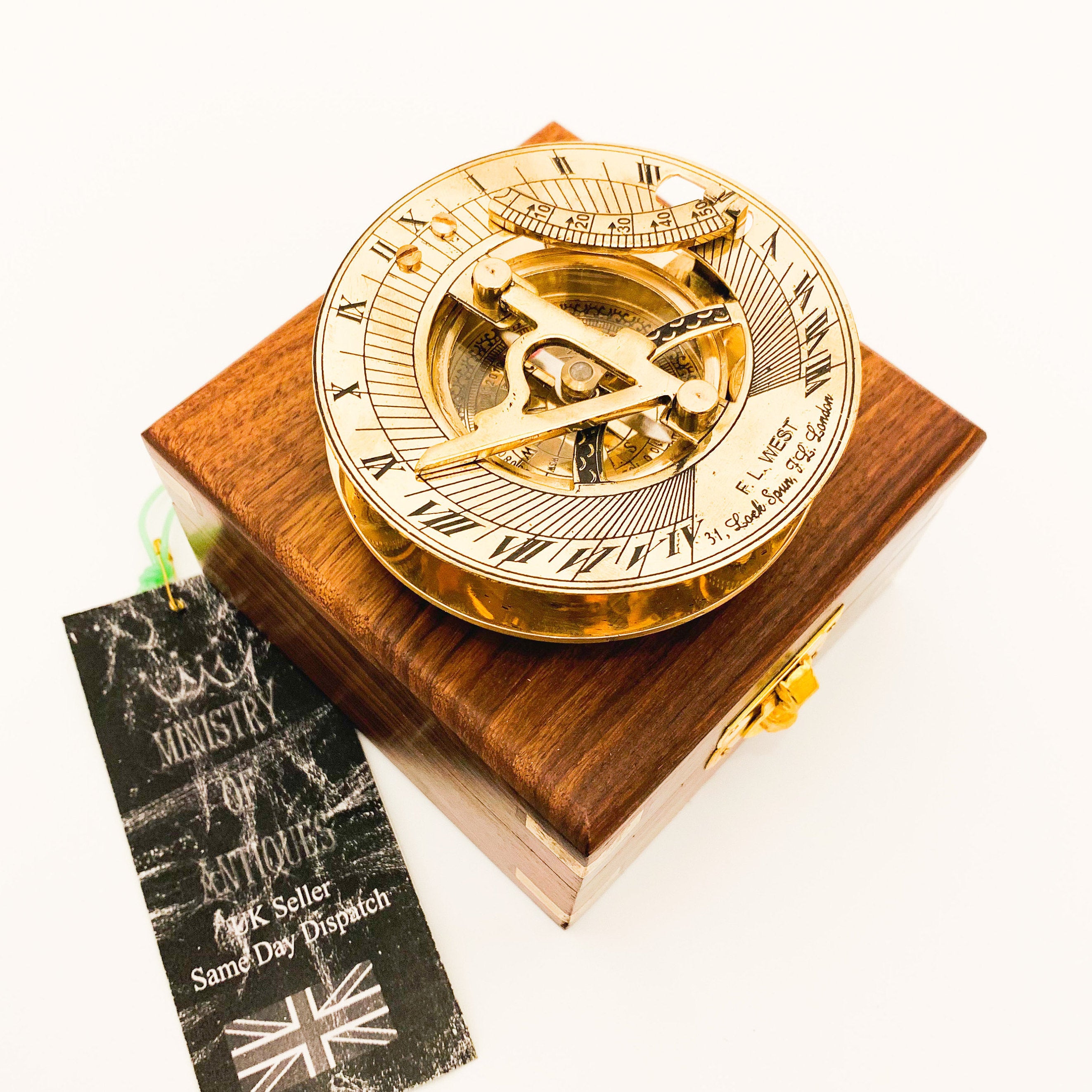 May include: A brass sundial with a compass in a wooden box. The sundial has Roman numerals and a compass rose. The box is made of dark wood and has a brass latch.