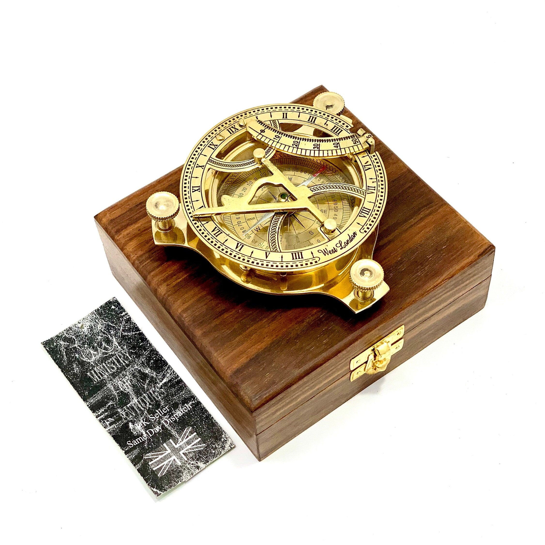May include: A brass compass with a wooden box. The compass features a sundial, a compass rose, and a time scale. The box is made of dark wood and has a brass latch.