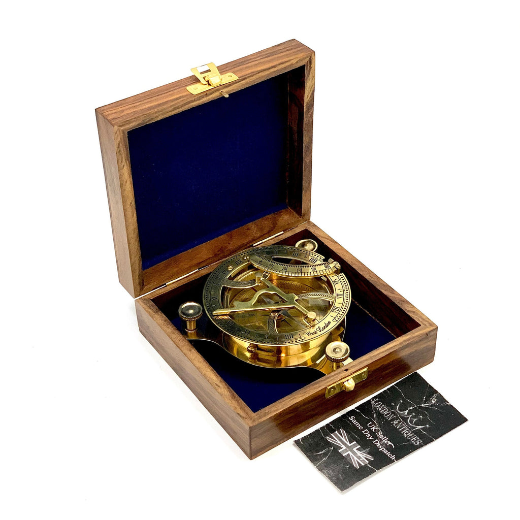 May include: A brass sundial with a compass in a wooden box. The sundial has a clear glass cover and is marked with Roman numerals. The box is made of dark wood with a blue velvet lining.