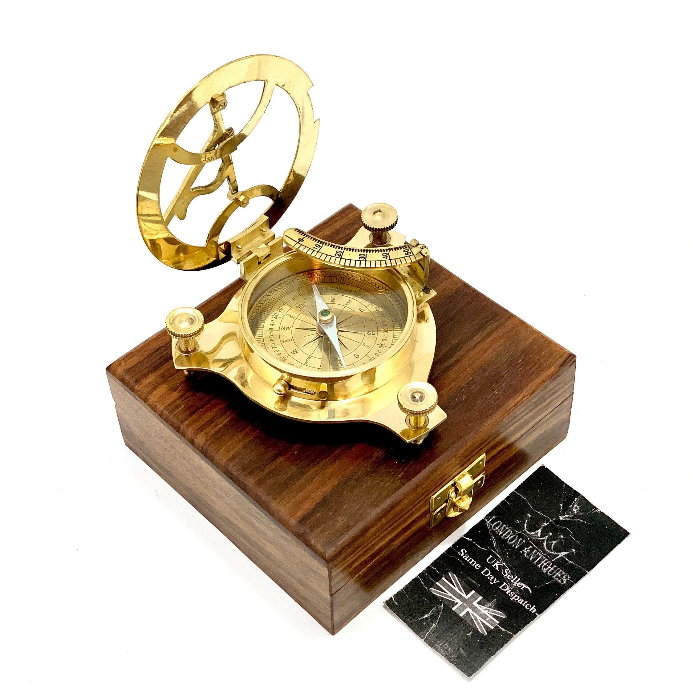 May include: A brass compass and sundial set in a wooden box. The compass features a gold face with black markings and a green needle. The sundial has a brass frame with a gold dial. The box is made of dark wood with a hinged lid.