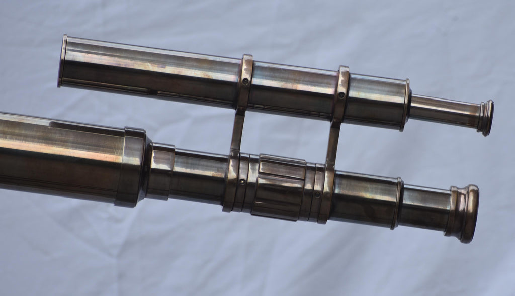 May include: A vintage brass telescope with two parallel tubes. The telescope has a classic design with multiple sections and rings. The brass has a warm, aged patina, suggesting it is an antique or a replica of an antique.