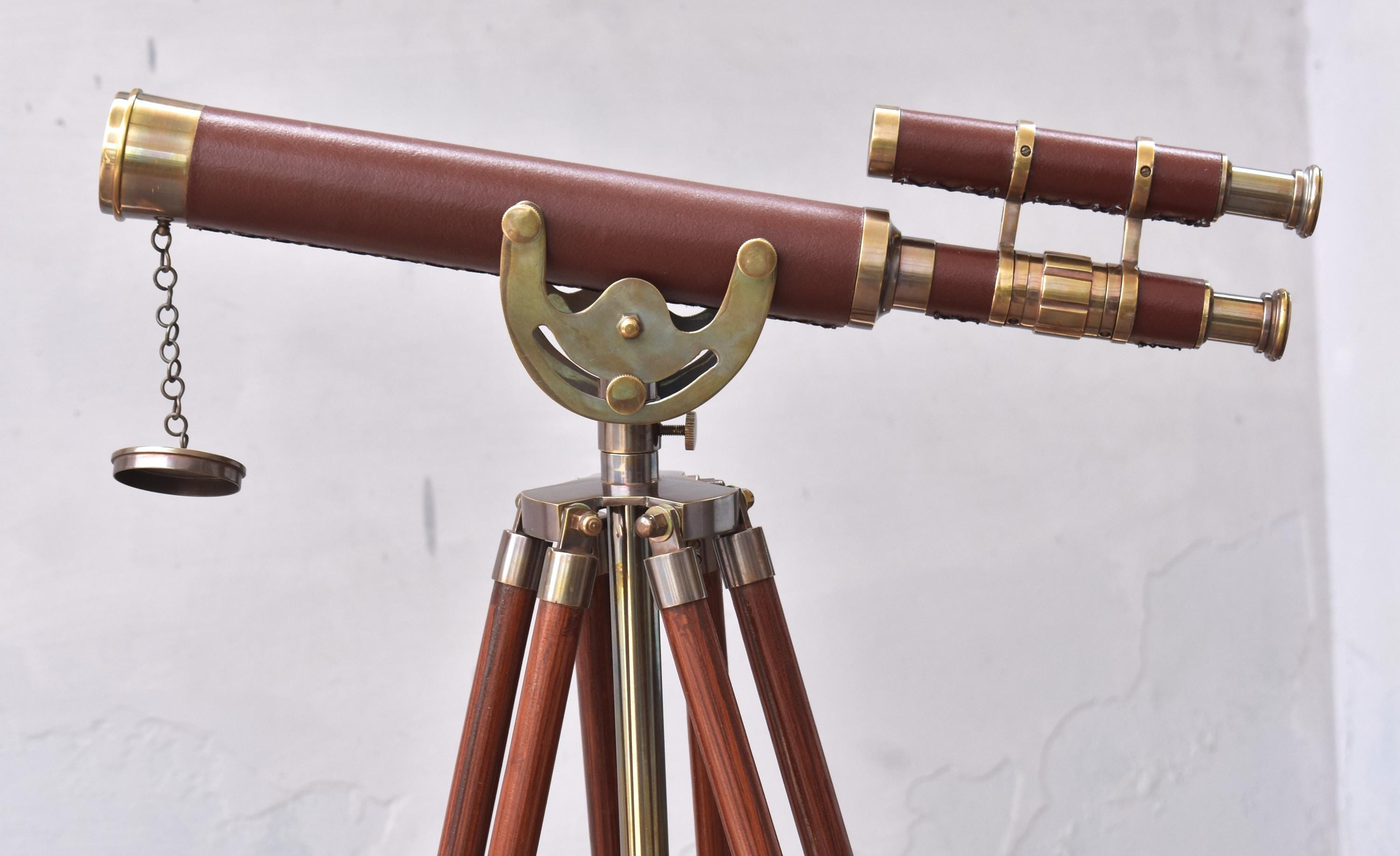 May include: A classic telescope featuring a brown leather-clad barrel and brass detailing. It is supported by a wooden tripod with brass elements. The telescope includes a secondary scope and a chained lens cover.