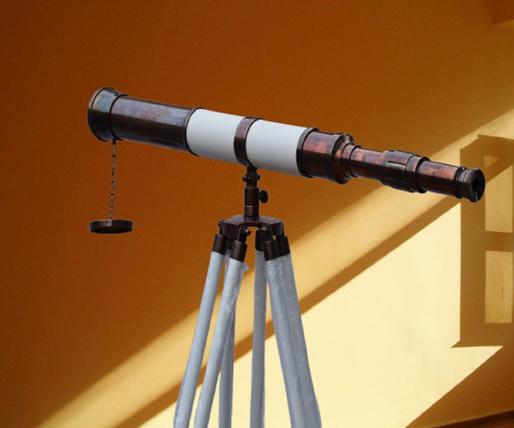 Può includere: Un telescopio in stile vintage con finitura bronzo e sezione centrale bianca. È montato su un treppiede con gambe grigio chiaro. Il telescopio ha un piccolo tappo rotondo attaccato da una catena.