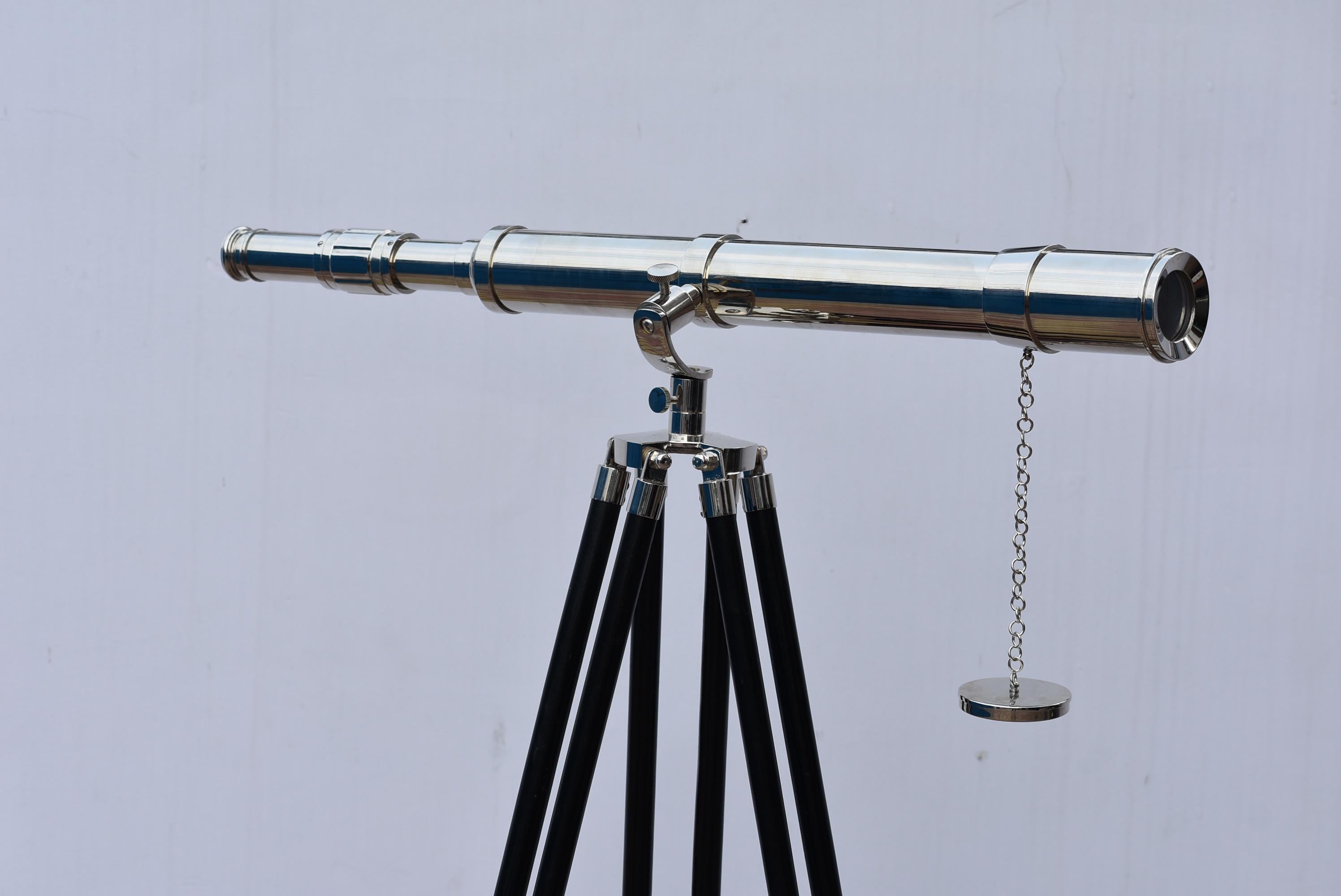 May include: A silver telescope on a black tripod. The telescope has a long, cylindrical body with adjustable focus. A small chain with a circular weight hangs from the barrel. The tripod legs are black, and the hardware is silver.