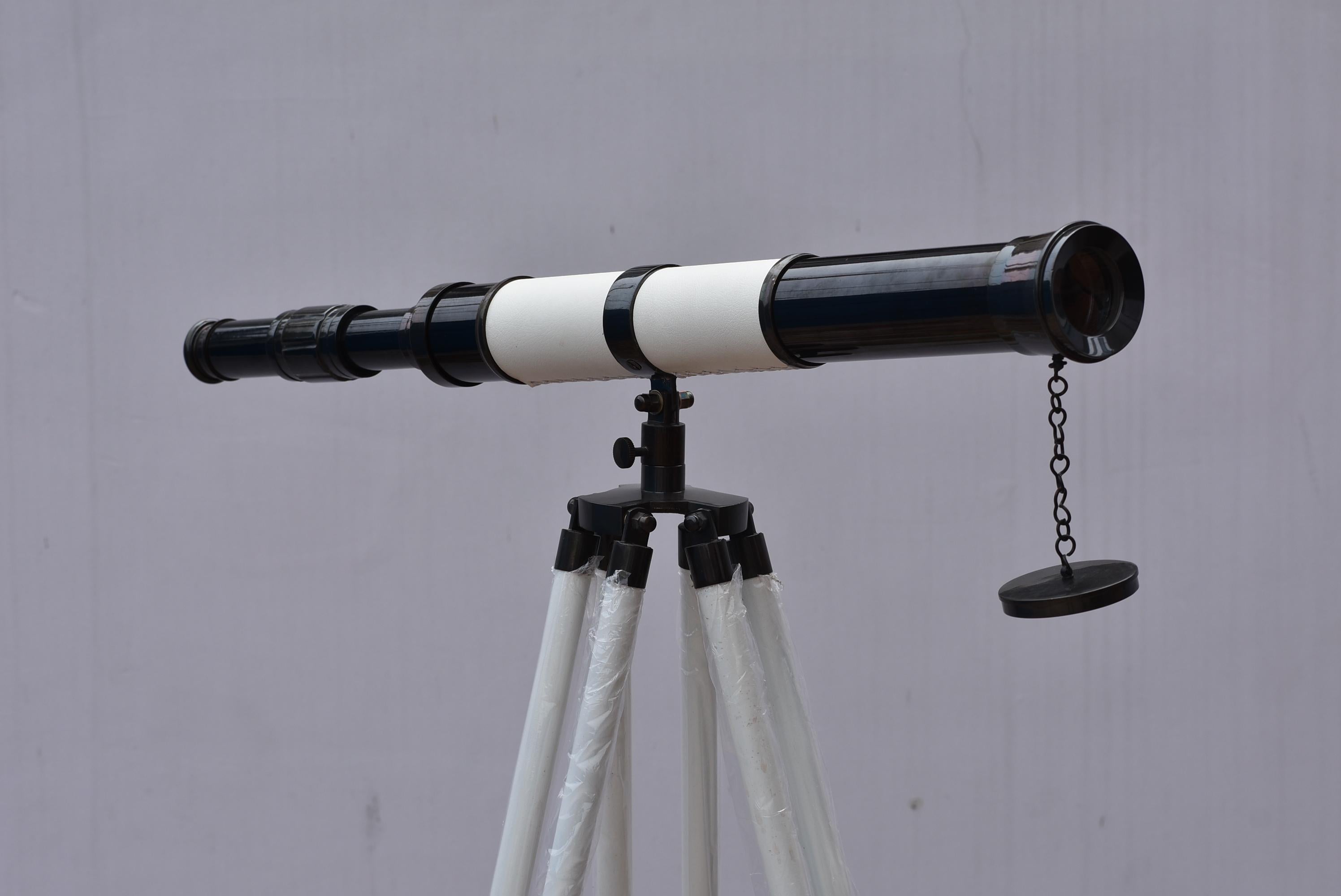 May include: A black and white telescope on a tripod stand. The telescope features a black body with white bands and a lens cap on a chain. The tripod has white legs and a black head.