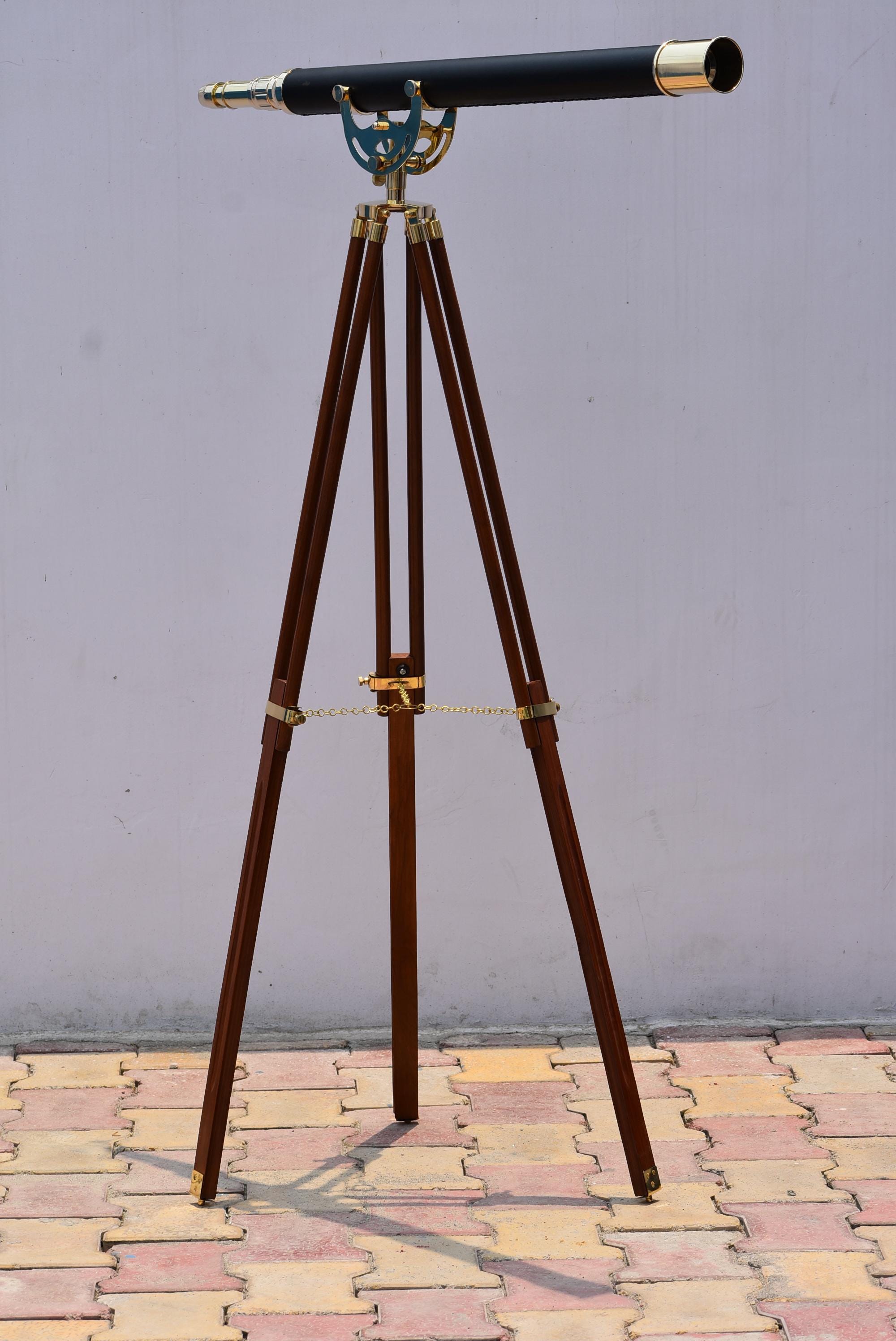 May include: A vintage-style telescope with a black barrel and brass accents, mounted on a dark brown wooden tripod. The tripod legs are adjustable and feature brass hardware. The telescope is a classic nautical or scientific instrument.