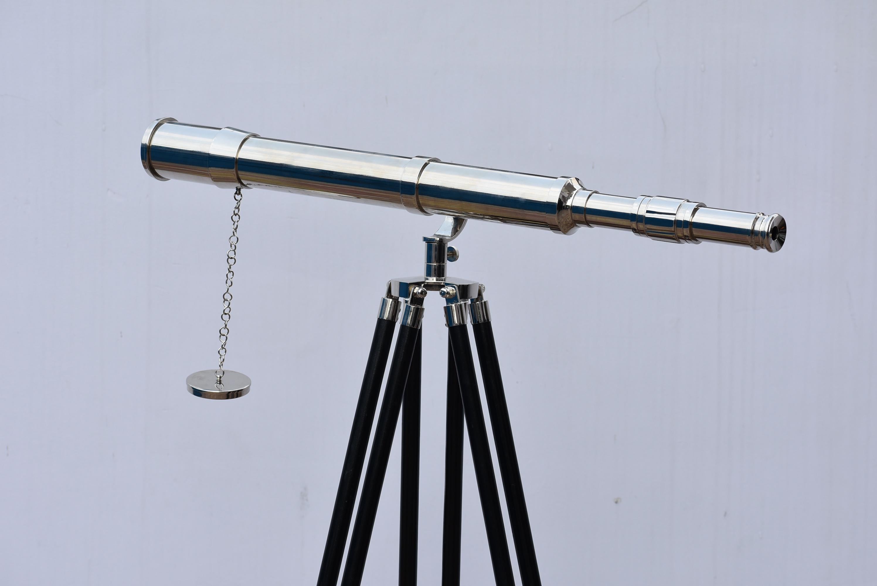 May include: A shiny silver telescope with a chain and a small circular weight, mounted on a black and silver tripod. The telescope is designed for viewing distant objects. The tripod has three black legs.