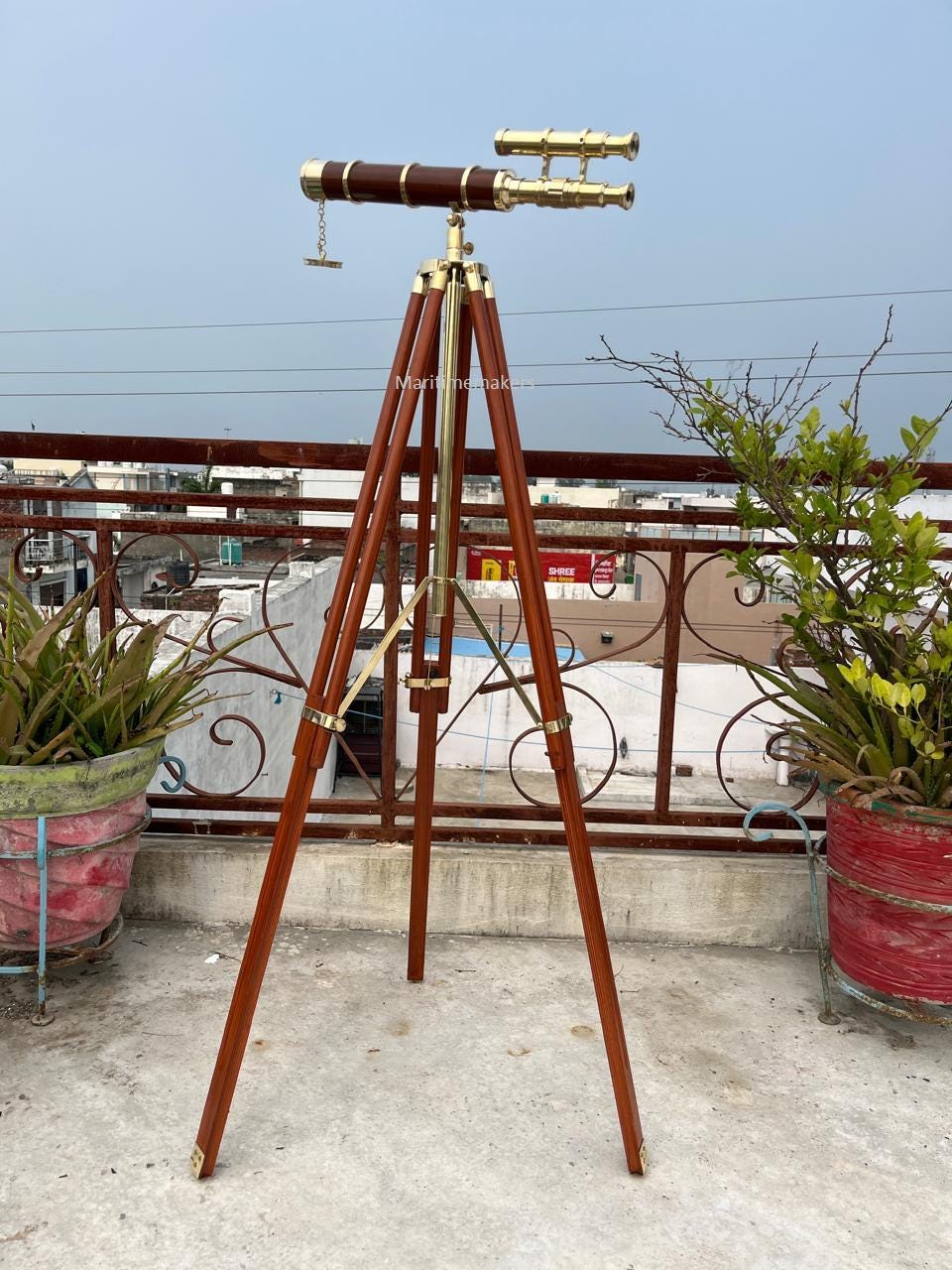 May include: A vintage telescope with a brass and brown finish, mounted on a wooden tripod. The telescope has a long, cylindrical barrel and a smaller, angled eyepiece. The tripod has adjustable legs and brass fittings.