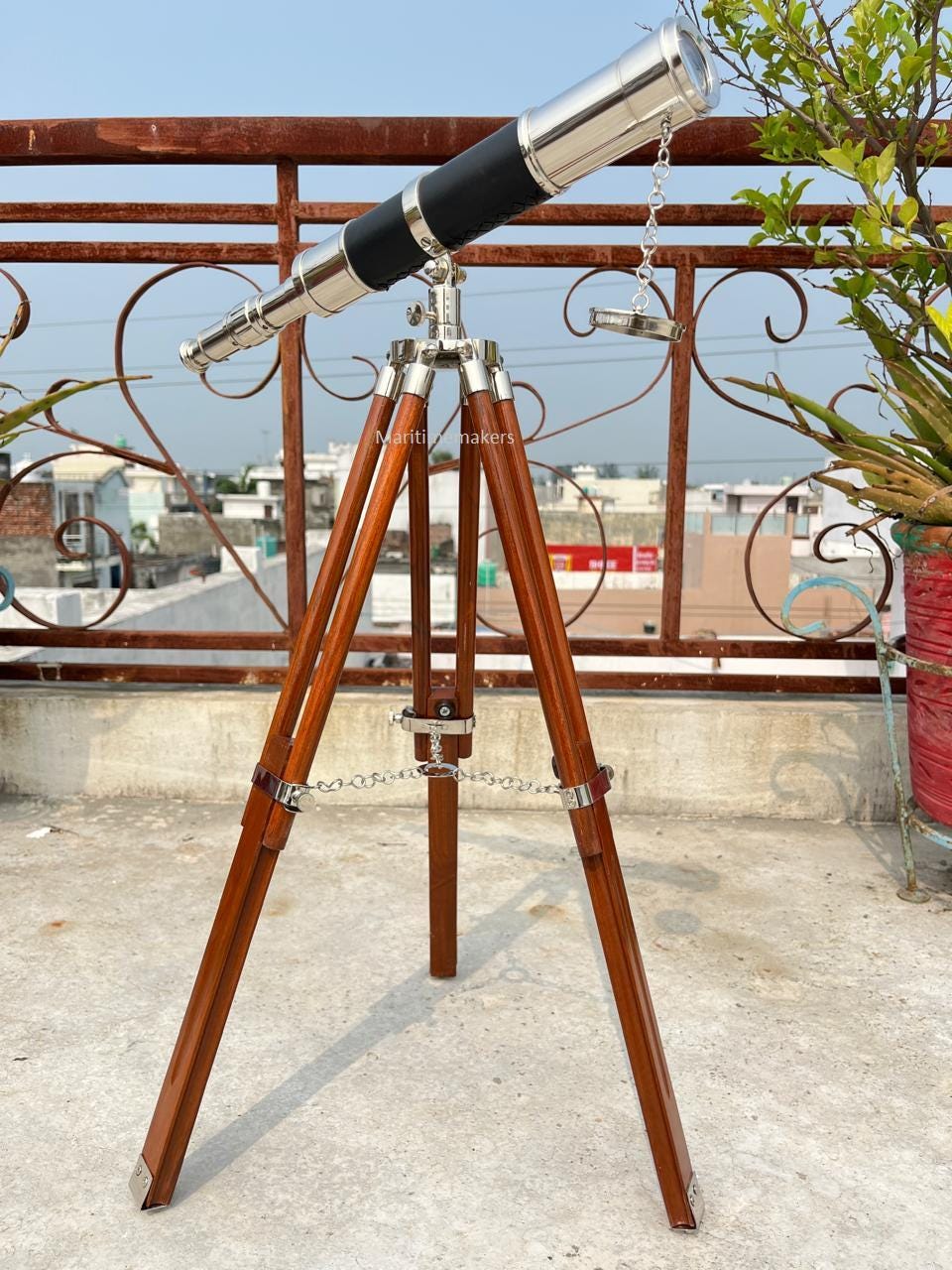 May include: A vintage-style telescope with a silver-colored barrel and black leather grip, mounted on a wooden tripod. The tripod has brown legs and metal accents. The text "Maritim makers" is visible on the base.