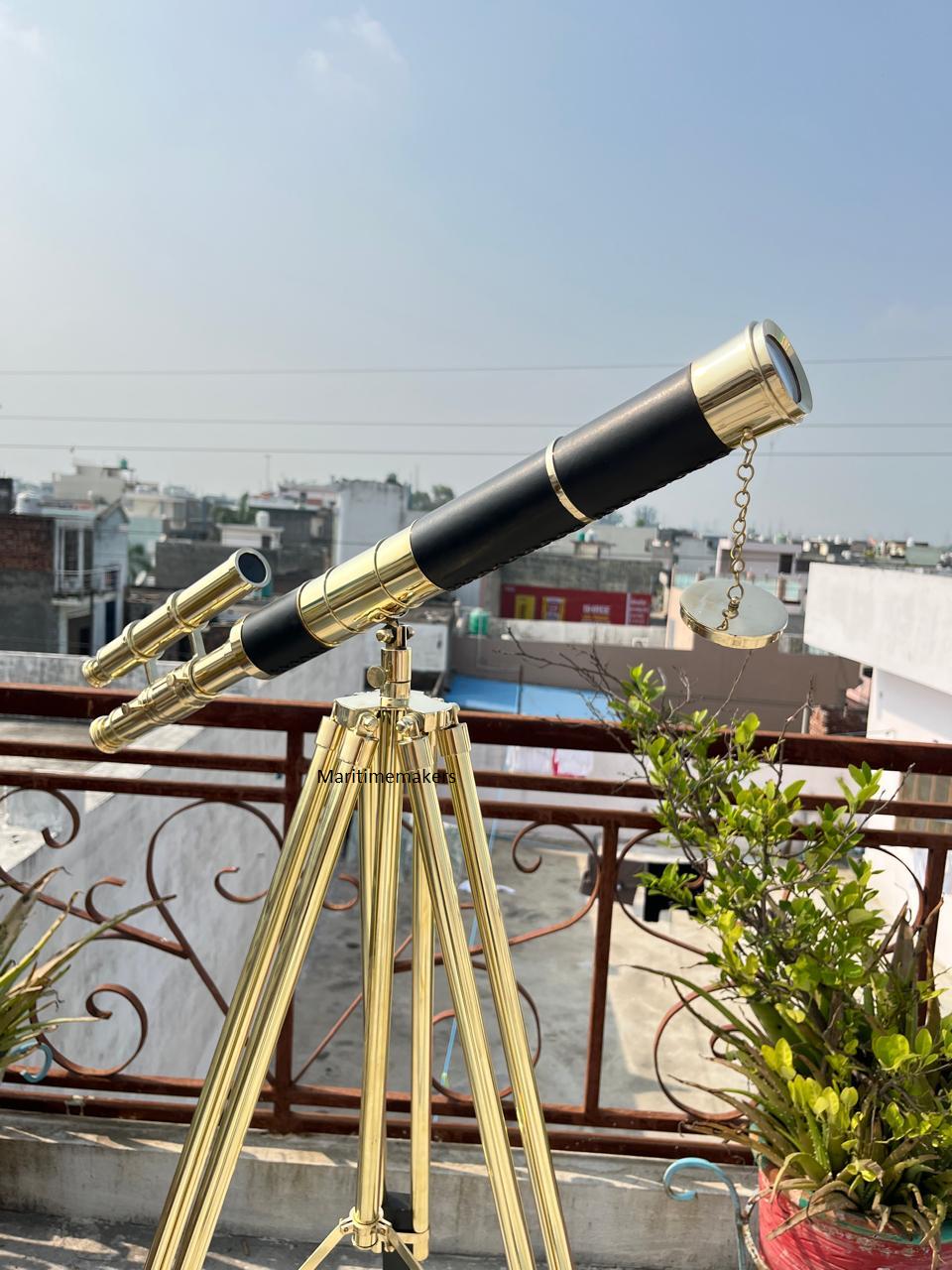 Può includere: Un telescopio nero e ottone montato su un treppiede in ottone. Il telescopio ha un corpo nero con dettagli in ottone e un piccolo mirino secondario. Il treppiede a tre gambe è posizionato all'aperto, con edifici e cielo blu sullo sfondo.