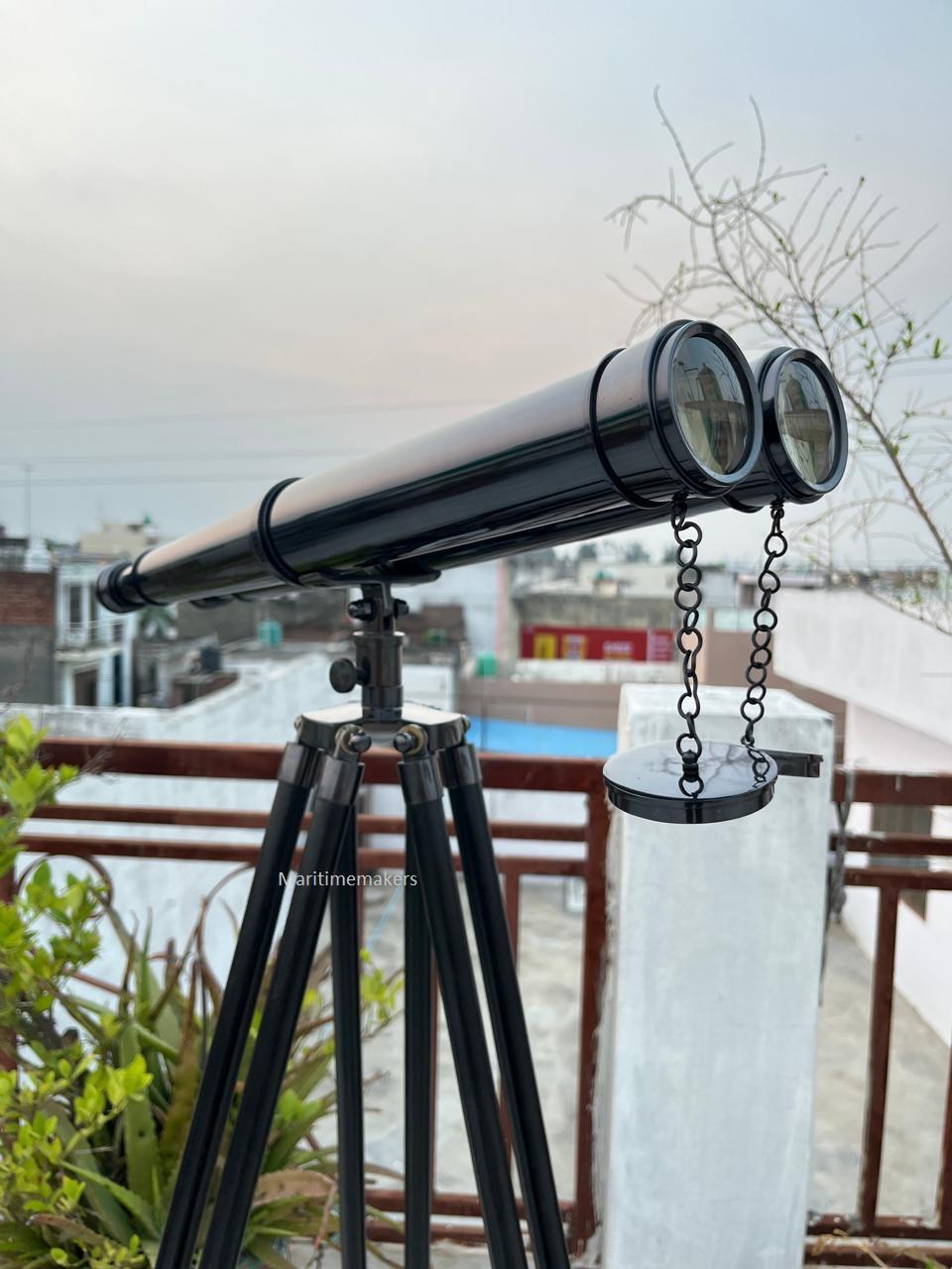 Può includere: Un telescopio nero con un treppiede. Il telescopio ha due lenti ed è collegato da una catena. Il treppiede ha tre gambe. Il testo "Maritimemakers" è visibile sul treppiede.