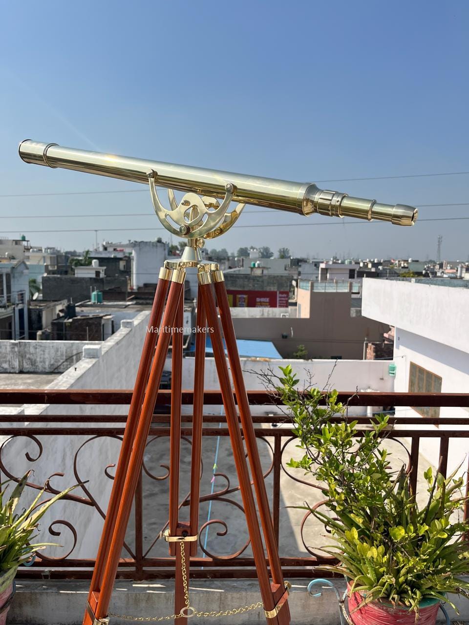 May include: A brass telescope mounted on a wooden tripod. The telescope has a long, cylindrical barrel and is supported by a decorative brass mount. The tripod legs are dark brown and the overall aesthetic is vintage.