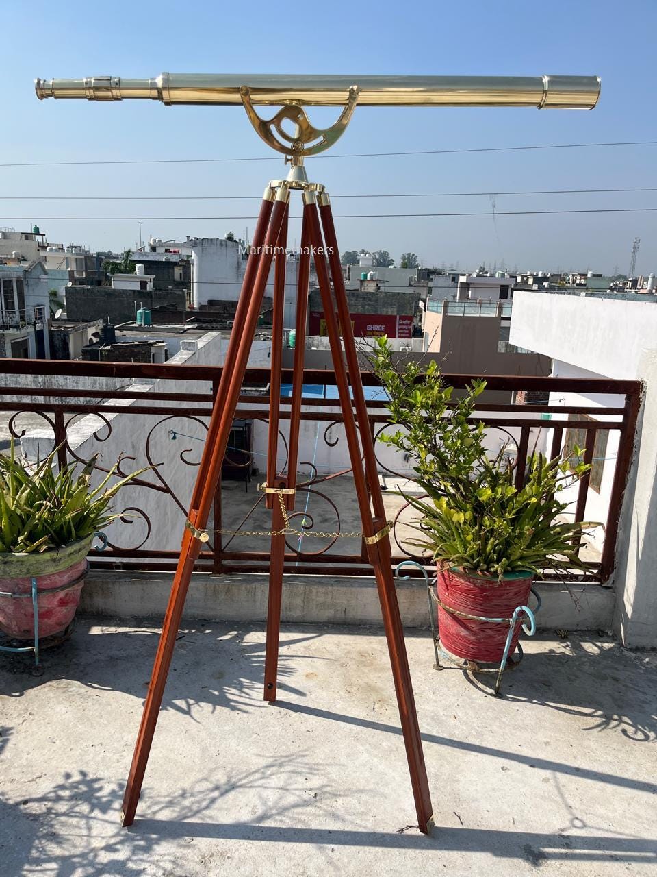 Può includere: Un telescopio in ottone montato su un treppiede in legno. Il telescopio ha una canna lunga e cilindrica ed è sostenuto da un supporto decorativo in ottone. Le gambe del treppiede sono marroni scuro e collegate con hardware in ottone.