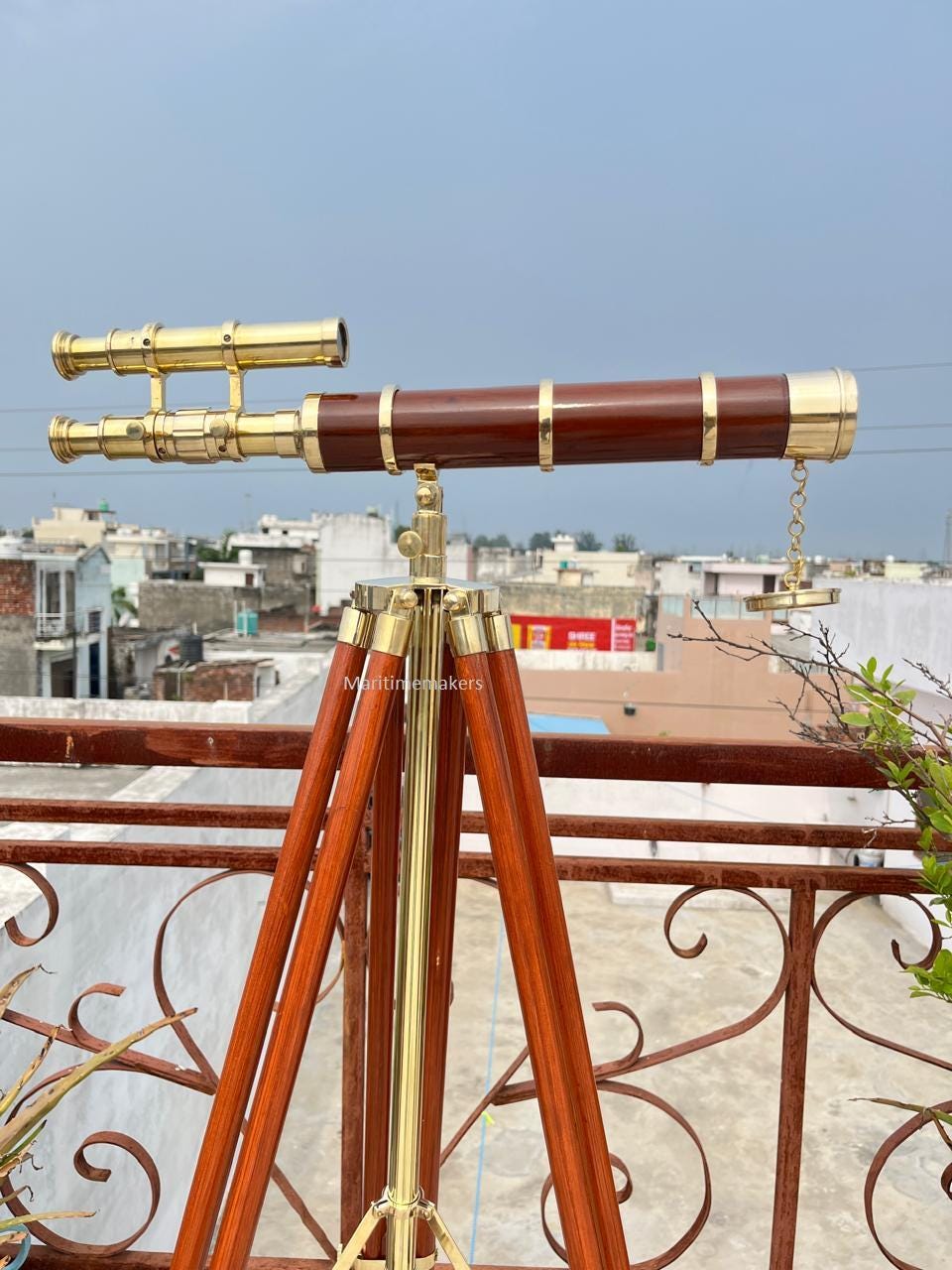 May include: A vintage telescope with a dark brown barrel and brass detailing, mounted on a wooden tripod. The telescope features a dual eyepiece and is designed for observation. The tripod legs are a rich, reddish-brown colour.