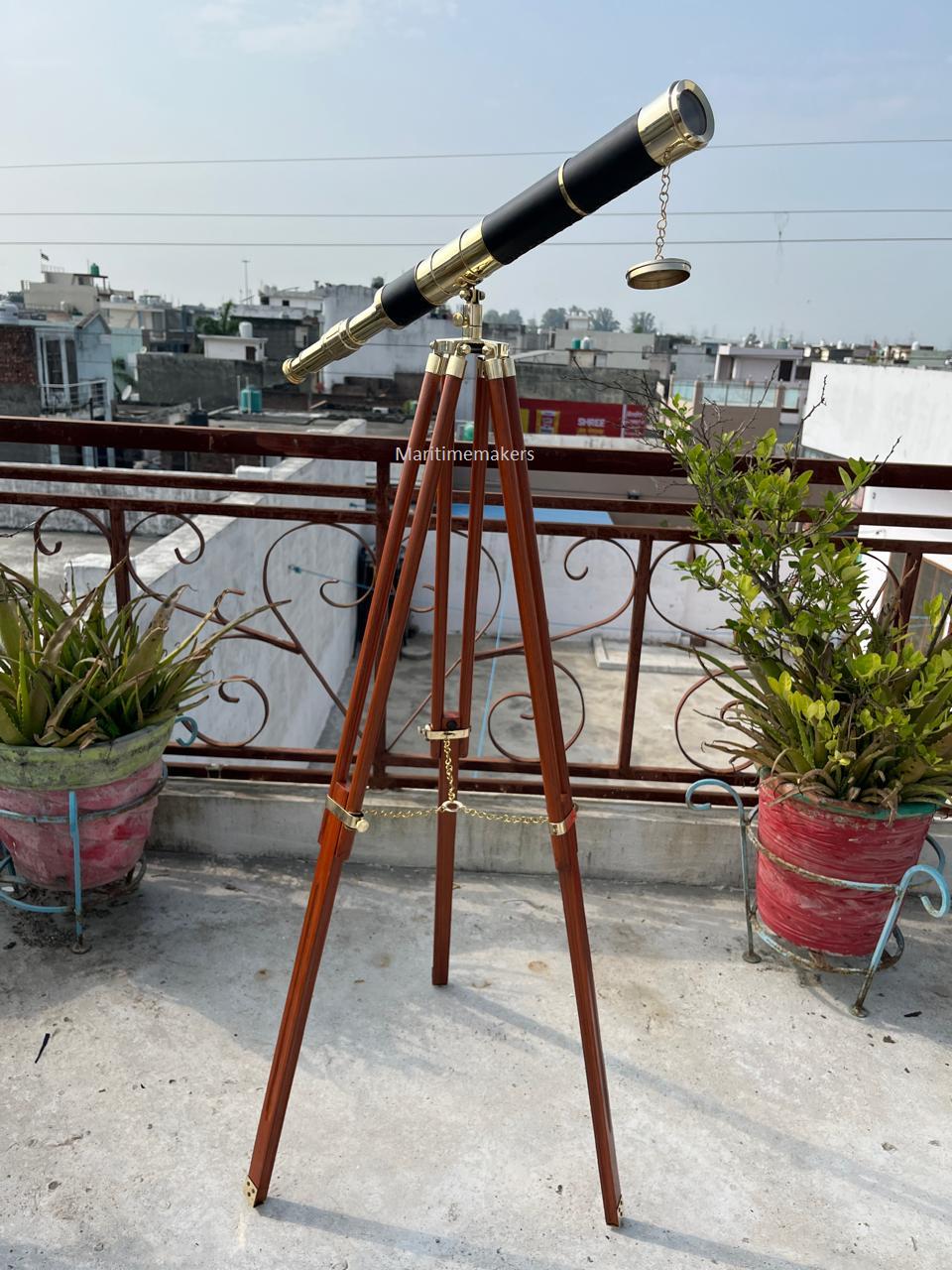 May include: A vintage telescope with a black and gold barrel, mounted on a wooden tripod. The telescope features brass accents and a chain-connected lens cap. The tripod legs are dark brown with brass fittings.