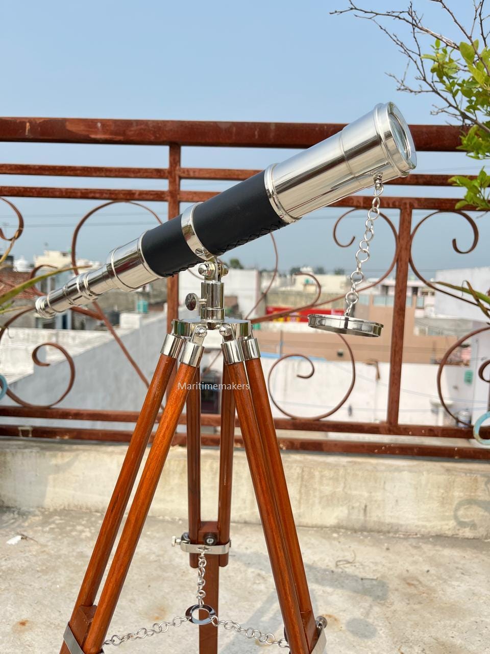 May include: A vintage-style telescope with a polished metal body and a black leather grip. It is mounted on a wooden tripod with metal accents. The telescope is designed for observation and exploration.
