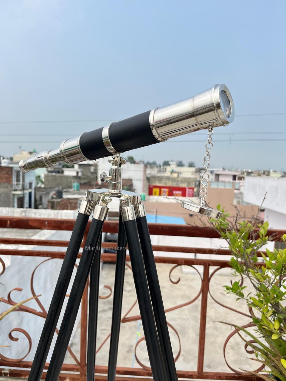 May include: A vintage-style telescope with a black leather-wrapped barrel and polished metal accents. It is mounted on a black wooden tripod with silver-colored metal fittings. The telescope is designed for observation.