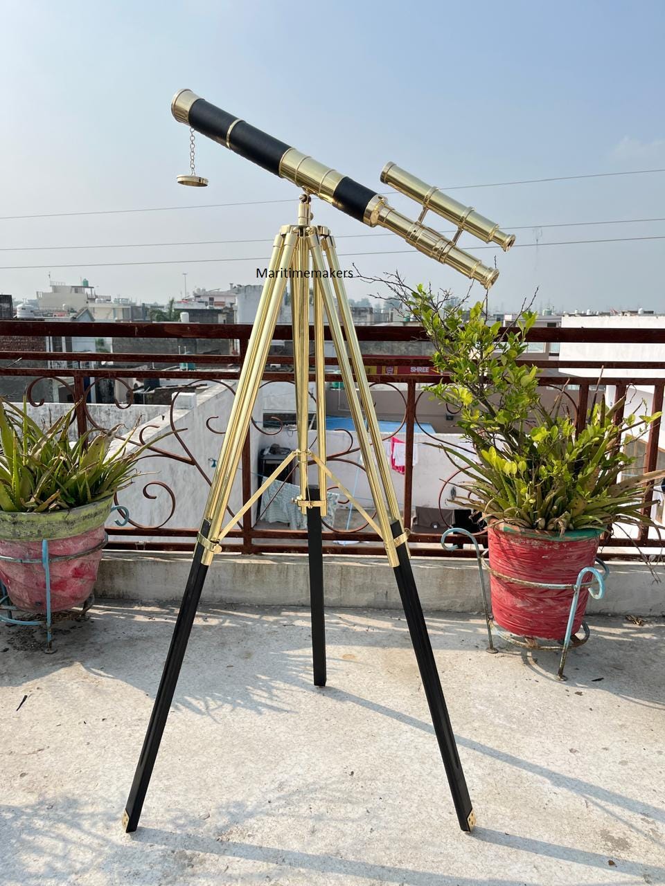 Può includere: Un telescopio in ottone e nero su un treppiede dorato. Il telescopio ha un corpo nero con dettagli dorati e un mirino più piccolo e parallelo. Le gambe del treppiede sono nere con elementi dorati. Il testo "Maritimemakers" è visibile.