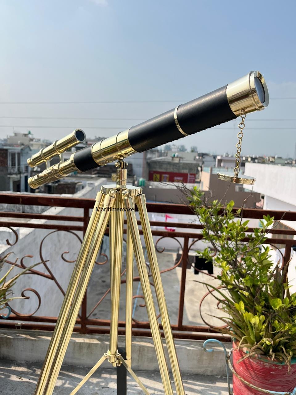 Può includere: Un telescopio in ottone con un tubo centrale nero e dettagli dorati, montato su un treppiede dorato. Il telescopio ha un secondo mirino più piccolo collegato. L'immagine è scattata all'aperto con un cielo sereno sullo sfondo.