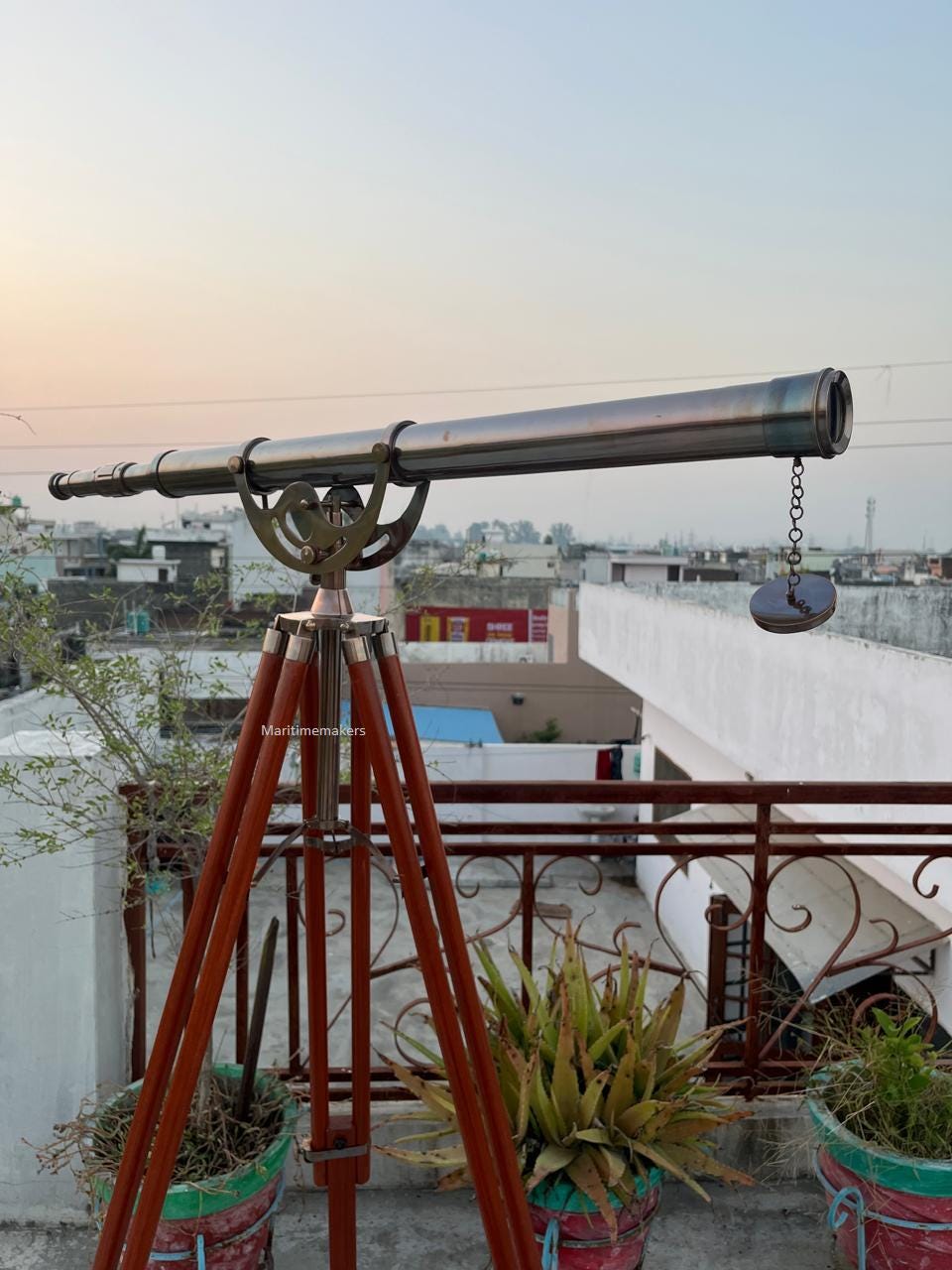 Può includere: Un telescopio in ottone in stile vintage montato su un treppiede in legno. Il telescopio ha una canna lunga e cilindrica ed è attaccato al treppiede con un'intricata lavorazione del metallo. Le gambe del treppiede sono di colore marrone scuro.