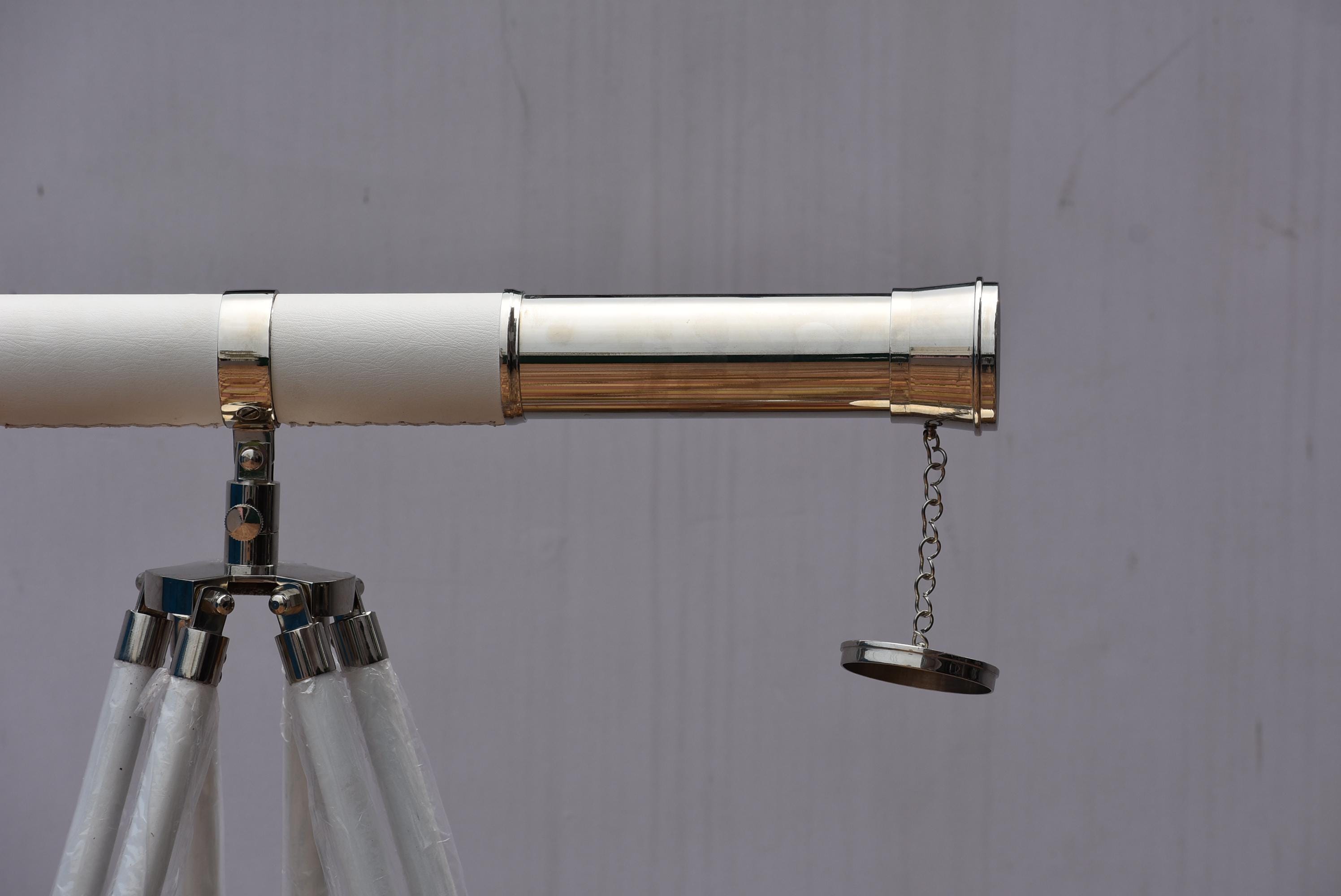 Può includere: Un telescopio bianco e argento su un treppiede argentato. Il telescopio ha un corpo bianco con dettagli argentati e un oculare argentato. Il treppiede ha gambe bianche e hardware argentato. Un oggetto nautico o decorativo.