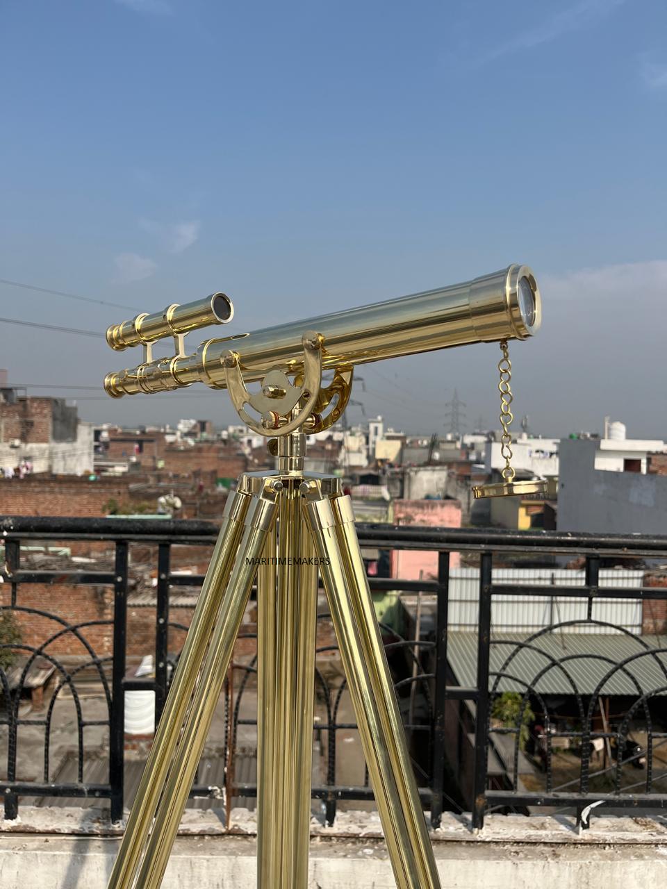 May include: A brass telescope on a tripod, set against a cityscape and blue sky. The telescope has a long barrel, an eyepiece, and a smaller sighting scope. The tripod has three legs. The text "MARITIMEMAKERS" is visible on the tripod.