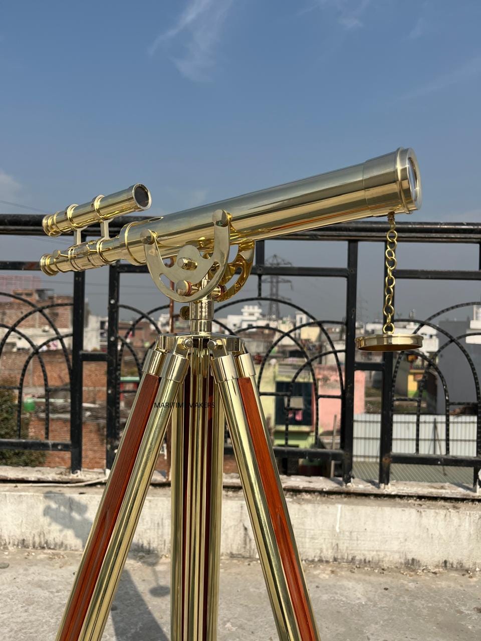 May include: A brass telescope with a wooden tripod. The telescope has a long, cylindrical barrel and a smaller eyepiece. The tripod has three legs with brass accents and wooden panels. The sky is blue in the background.
