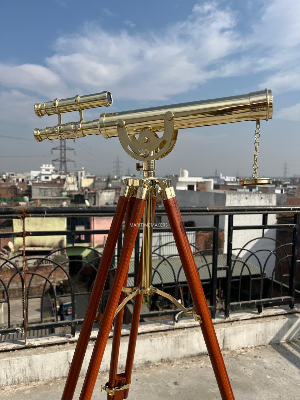 May include: A brass telescope with a wooden tripod. The telescope has a long barrel and a smaller, parallel scope. The tripod legs are dark brown and the metal components are gold-colored. The telescope is designed for viewing distant objects.